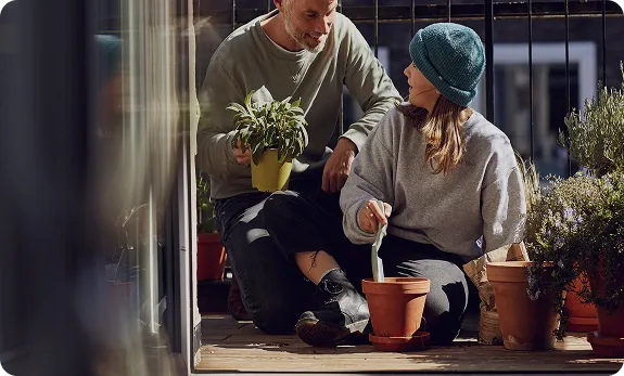 Mand og kvinde planter blomster i potter sammen på en terrasse i dagslys.