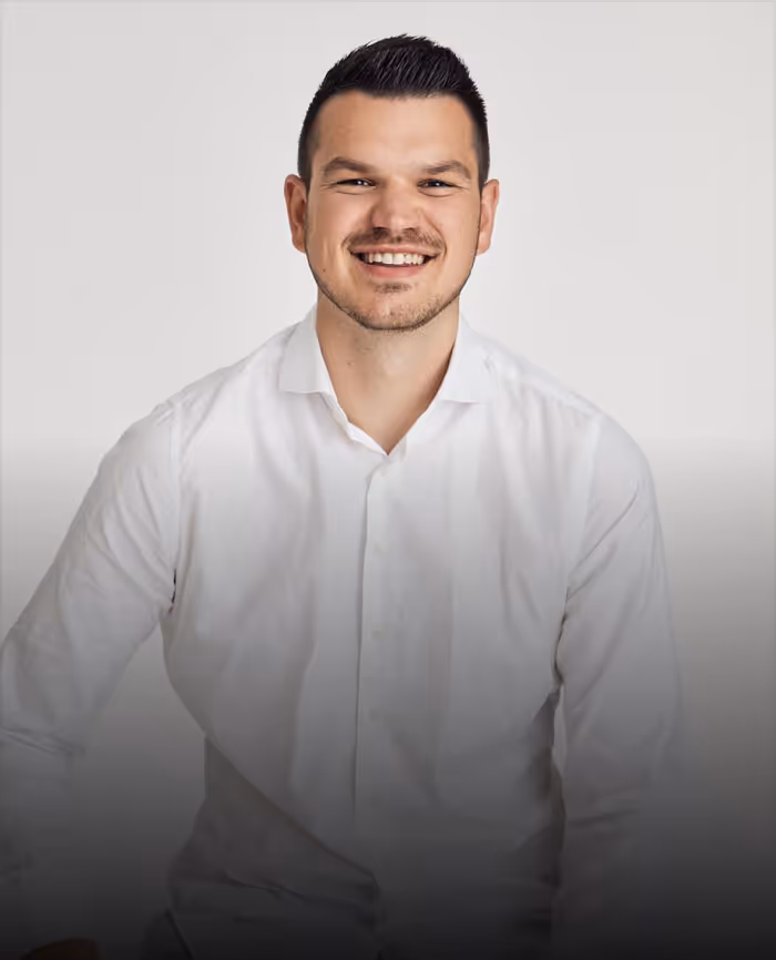 Smiling Max Klemmer with short dark hair wearing a white button-up shirt against a plain light background.