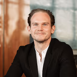 Robin Binder, NAO CEO, smiling man with short brown hair wearing a black blazer and white shirt, sitting indoors.