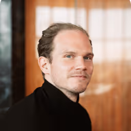 Robin Binder, NAO CEO, portrait of a man with light skin and slicked-back hair wearing a black turtleneck, looking slightly to the side.