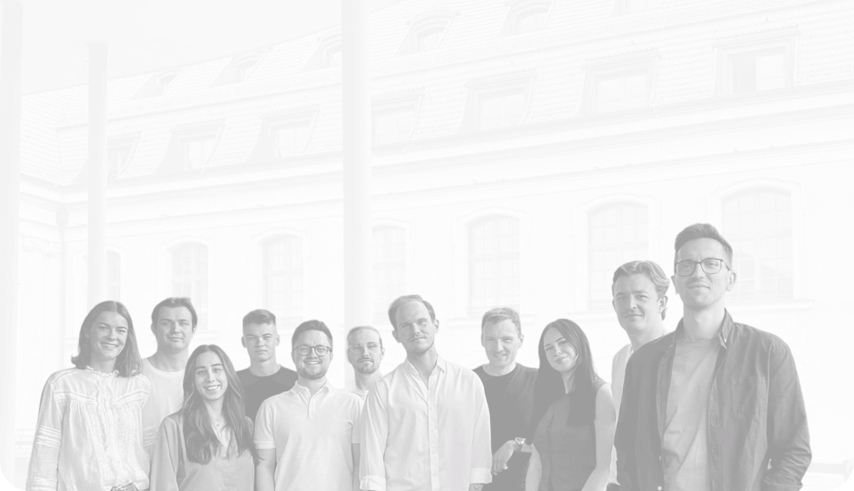 Gruppenbild von zehn jungen Erwachsenen, die vor einem Gebäude mit großen Fenstern stehen und in die Kamera lächeln.