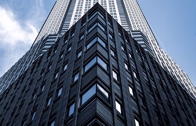 Blick nach oben auf ein modernes, schwarzes Hochhaus mit vielen Fenstern vor blauem Himmel.