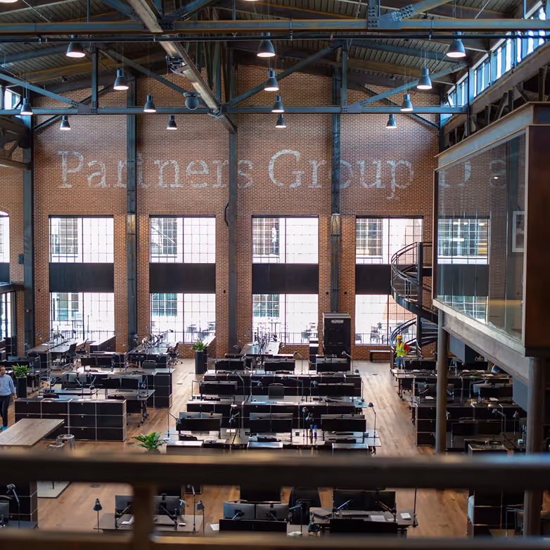 Großes offenes Büro mit vielen Schreibtischen vor Wand mit Partners Group Schriftzug.