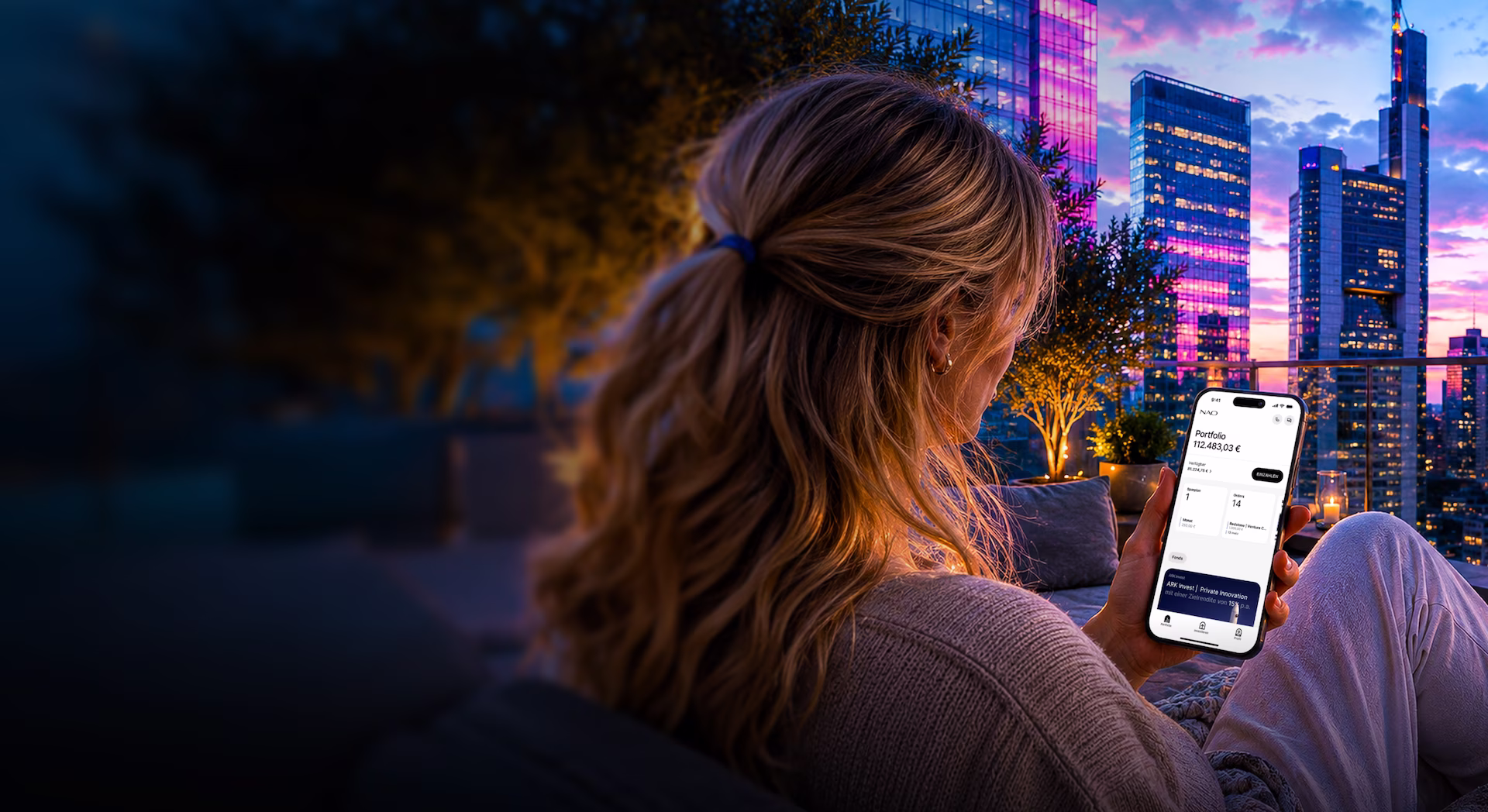 Frau sitzt abends auf Terrasse und sieht auf Smartphone ihr Portfolio mit 112.483,03 € vor Skyline.