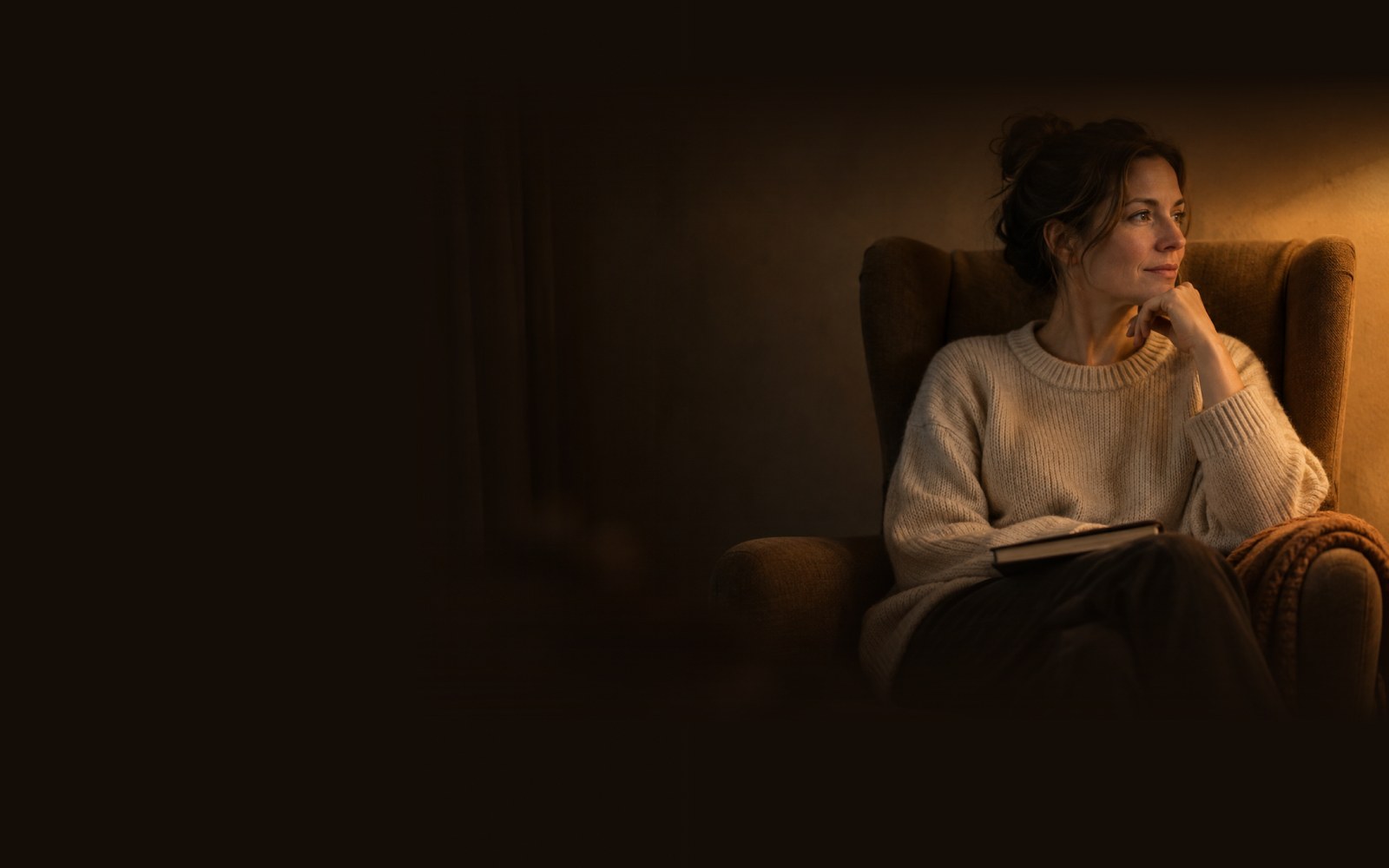 Frau sitzt abends nachdenklich in einem Lesesessel (KI-generiertes Bild)
