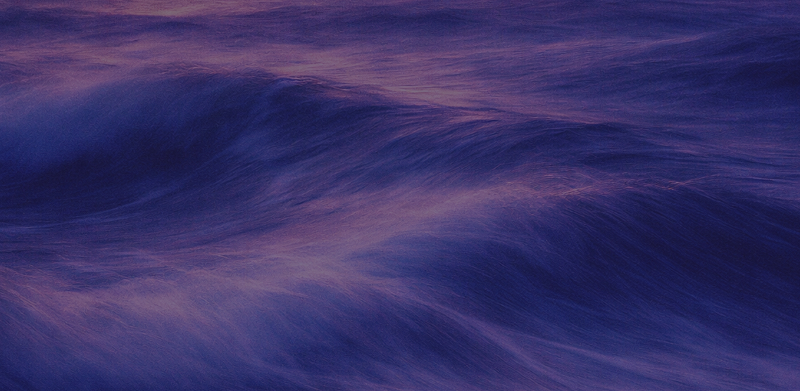 Soft, blurred close-up of ocean waves in purple and blue tones.