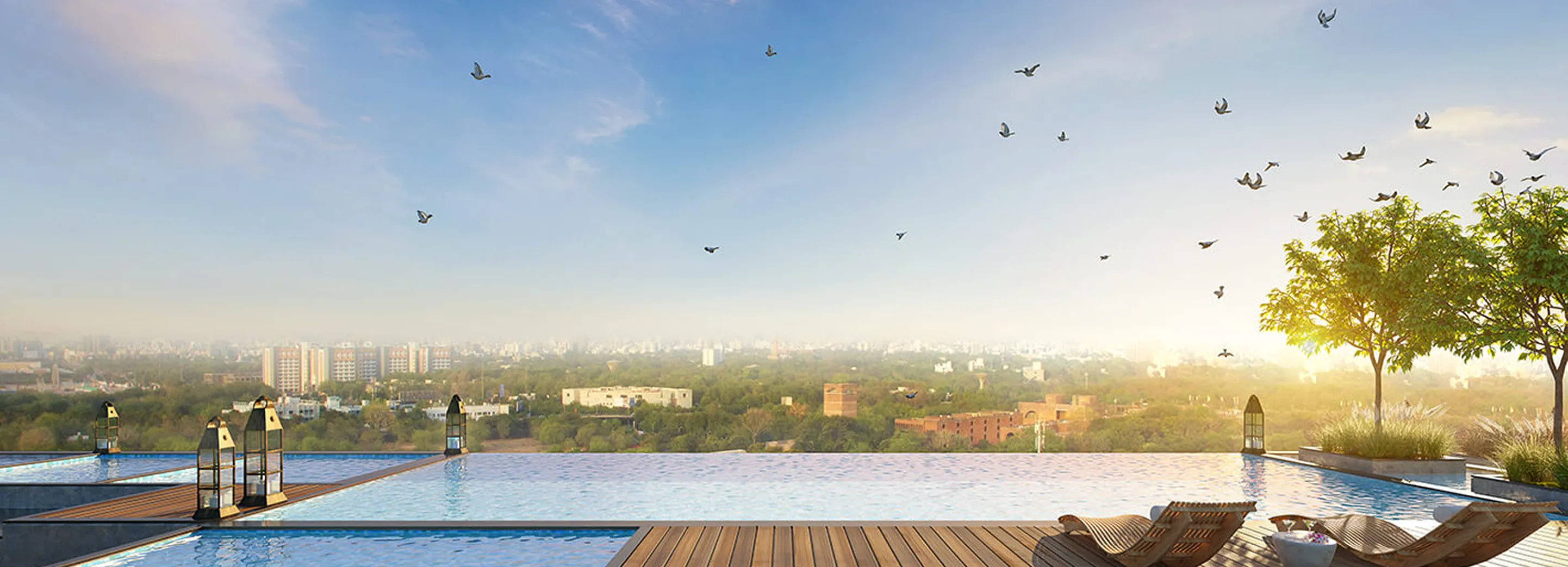 Infinity pool with wooden deck, lounge chairs, and lanterns overlooking a cityscape with trees and birds flying under a clear sky at sunset.