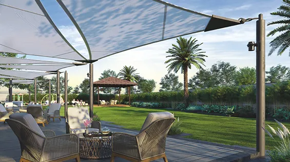 Outdoor patio area with wicker chairs, small table, large shade sails, and green lawn with palm trees in the background.