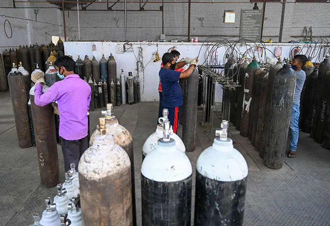 Workers in a warehouse wearing masks handling large oxygen cylinders stored upright.