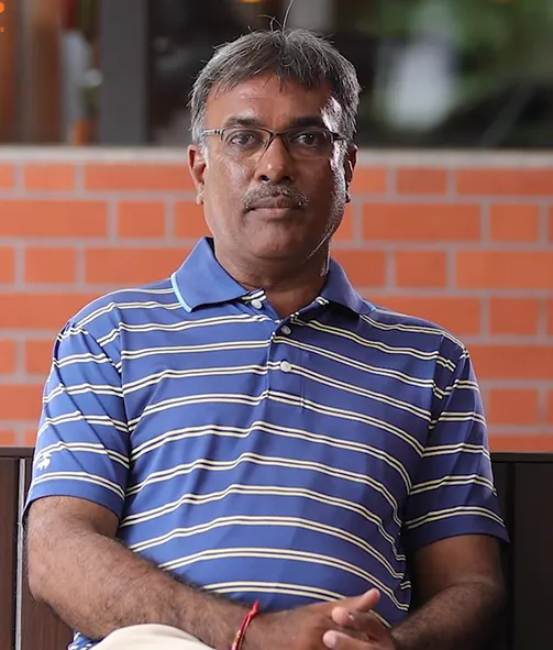 Middle-aged man with glasses wearing a blue and white striped polo shirt sitting in front of a brick wall.