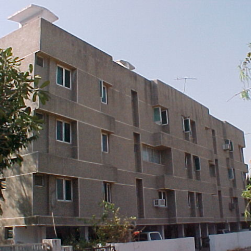 Three-story rectangular apartment building with multiple windows and air conditioning units on the facade.