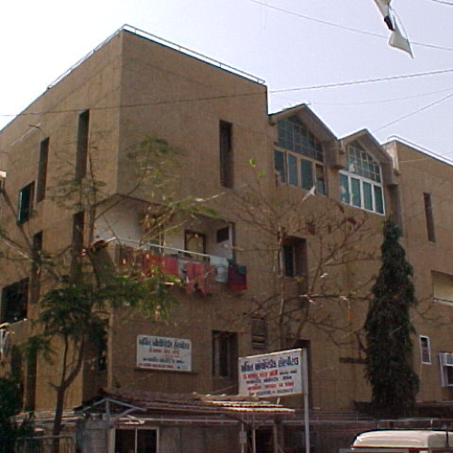 Three-story residential building with clothes hanging on a balcony and two signboards in front.