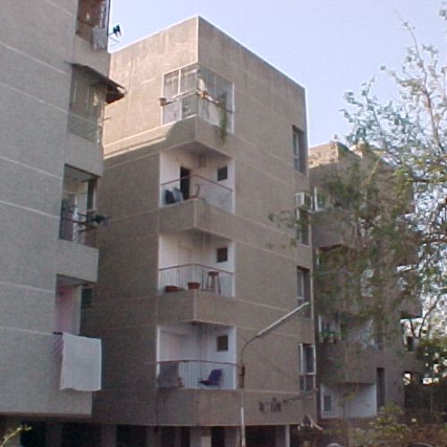 View of a beige residential apartment building with balconies, some chairs, and hanging laundry under a clear sky.