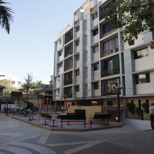Playground with swings and slides outside a multi-story residential building under clear sky.