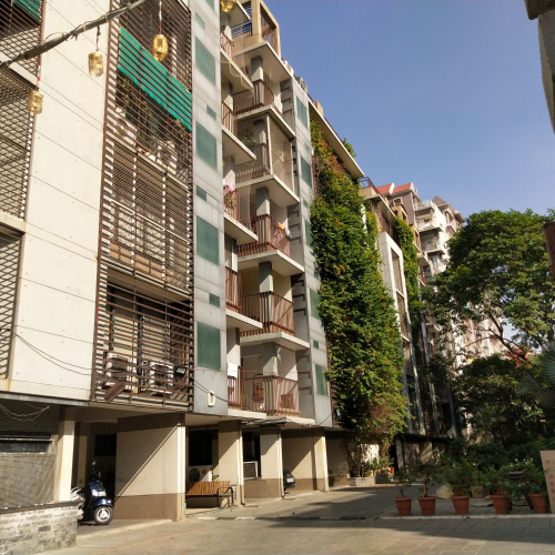 Multi-story apartment building with balconies, green vertical plants on the wall, potted plants, and a clear blue sky.