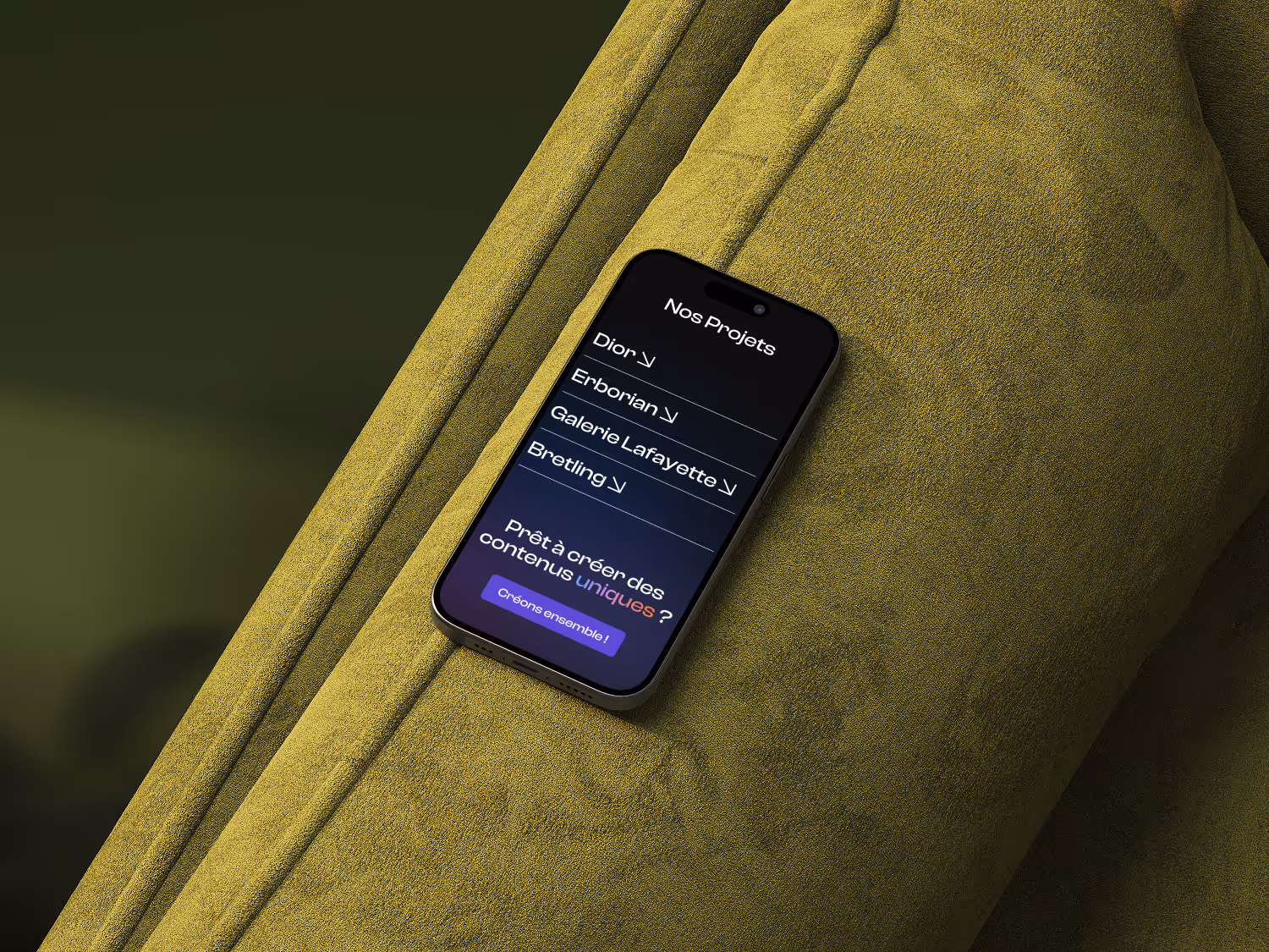 Smartphone resting on a green textured fabric with a screen showing Scob website with a project list including Dior, Erborian, Galerie Lafayette, and Breitling.