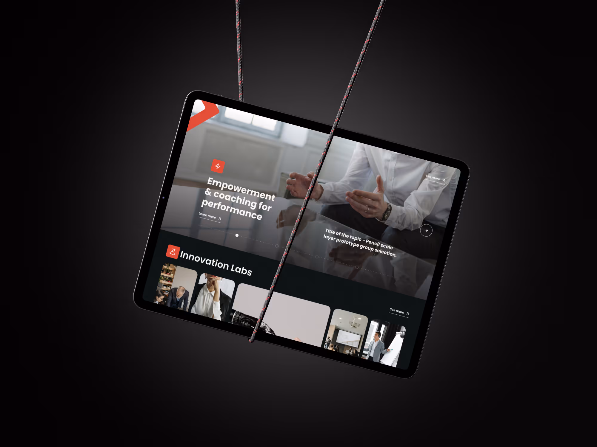 Tablet suspended by two cords displaying a aspelian website with sections titled 'Empowerment & coaching for performance' and 'Innovation Labs' on a dark background.