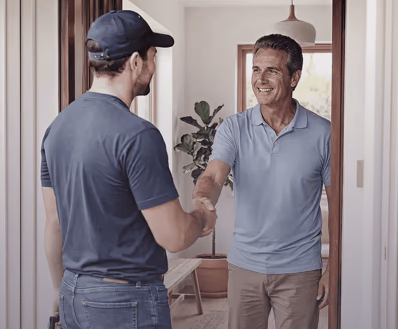 Un homme souriant en polo bleu serre la main d'un livreur portant une casquette et un t-shirt bleu.
