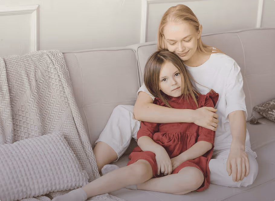 Jeune femme assise sur un canapé embrassant une petite fille portant une robe rouge.