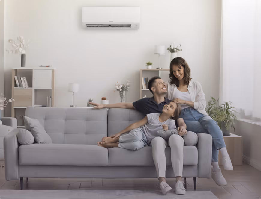 Une famille heureuse avec un père, une mère et leur fille assis sur un canapé gris dans un salon lumineux et moderne.