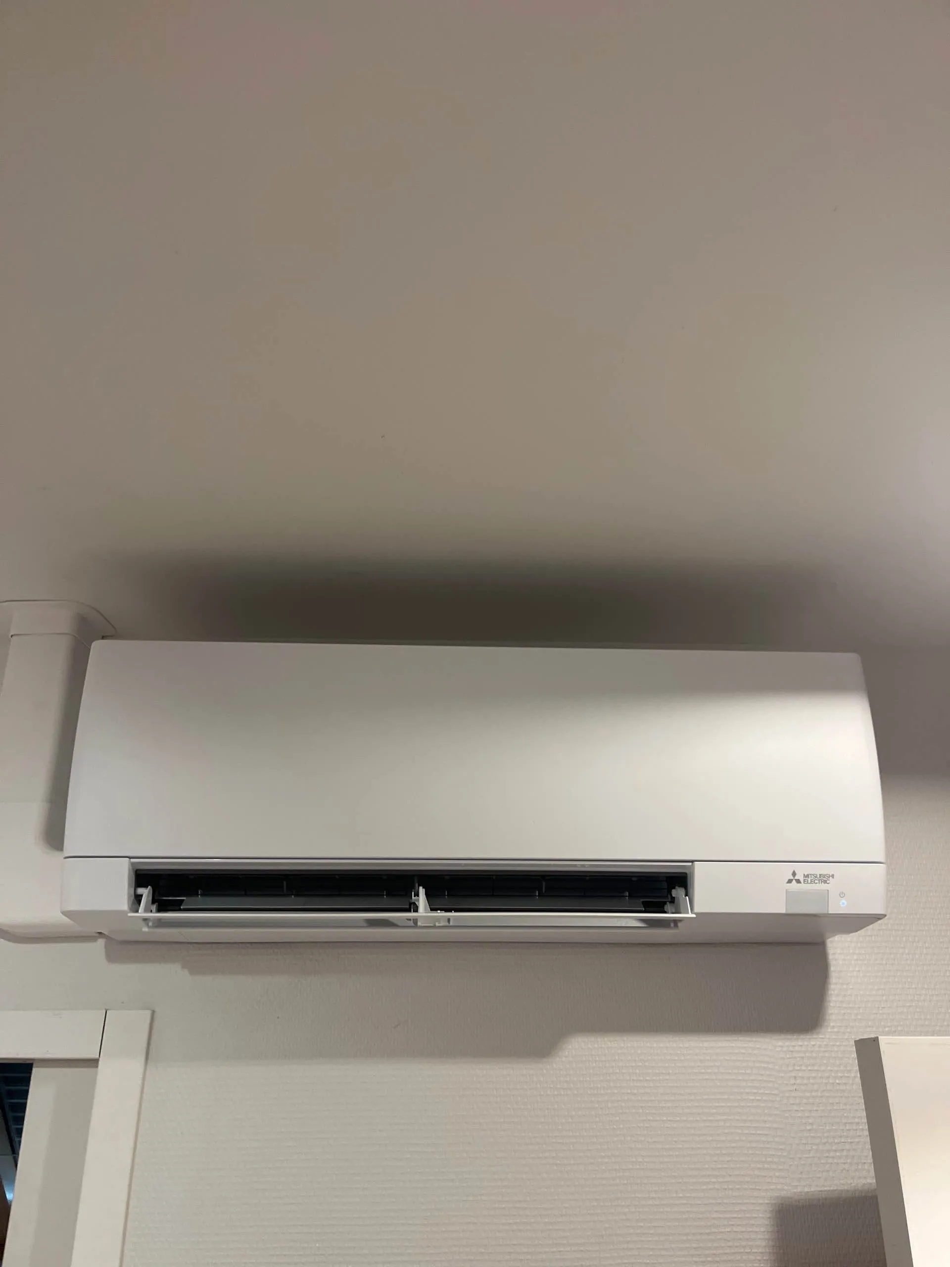 Climatiseur mural blanc Mitsubishi Electric installé au-dessus d'une porte dans une pièce intérieure.