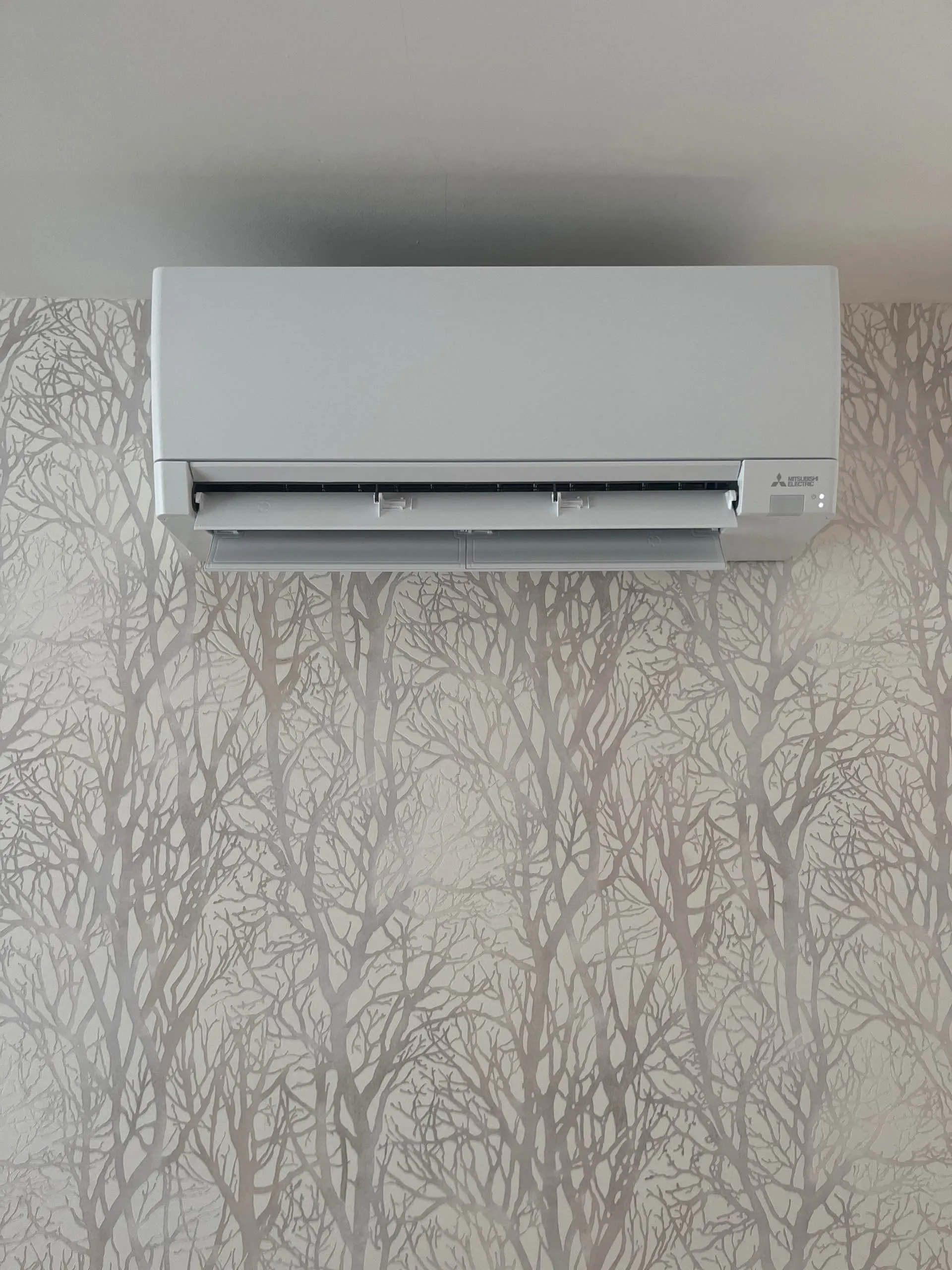 Unité murale de climatisation Mitsubishi Electric installée sur un mur avec un papier peint à motif d'arbres sans feuilles.