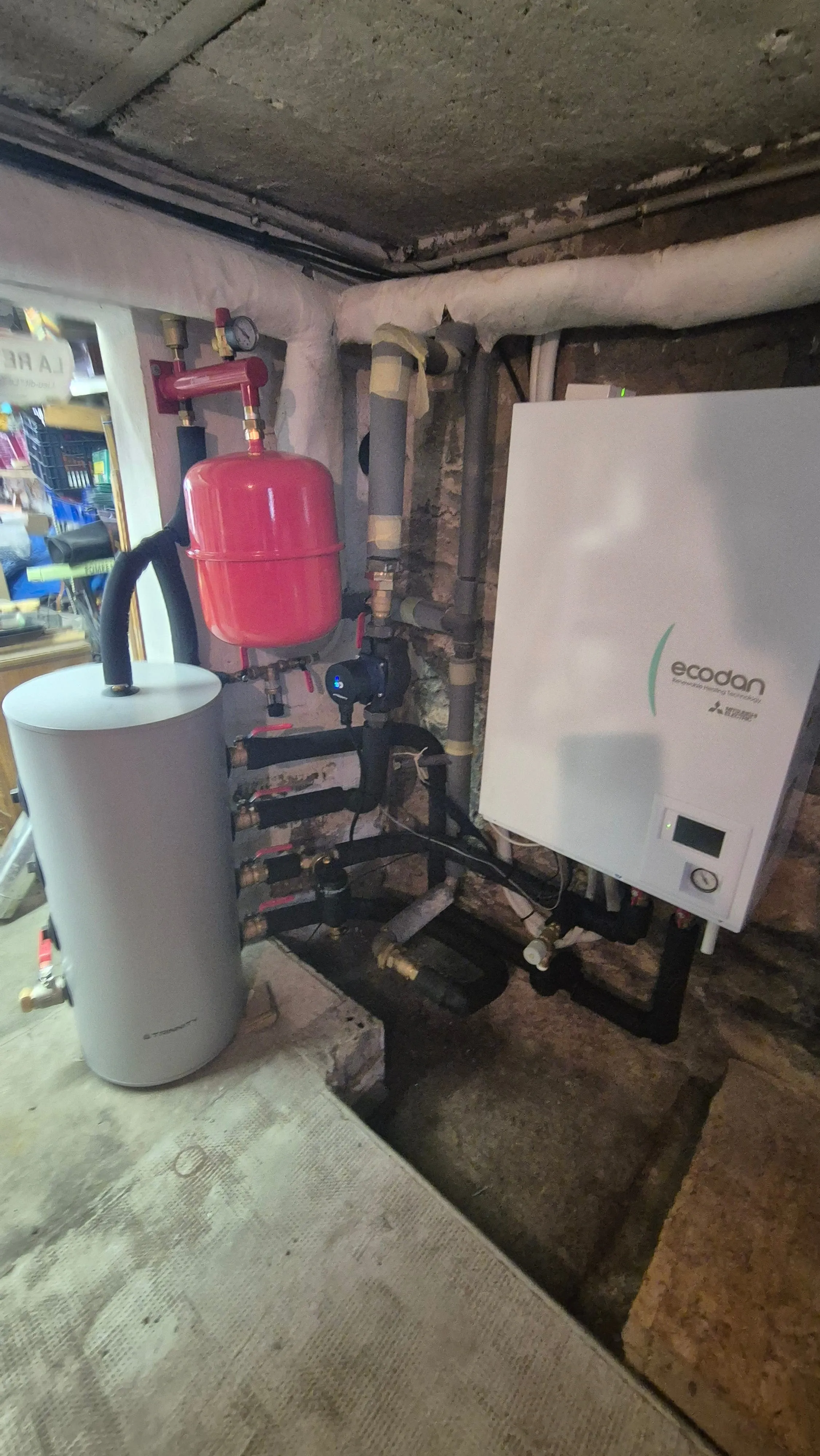 Installation de chaudière et ballon d'eau chaude avec tuyaux isolés dans une cave en pierre.