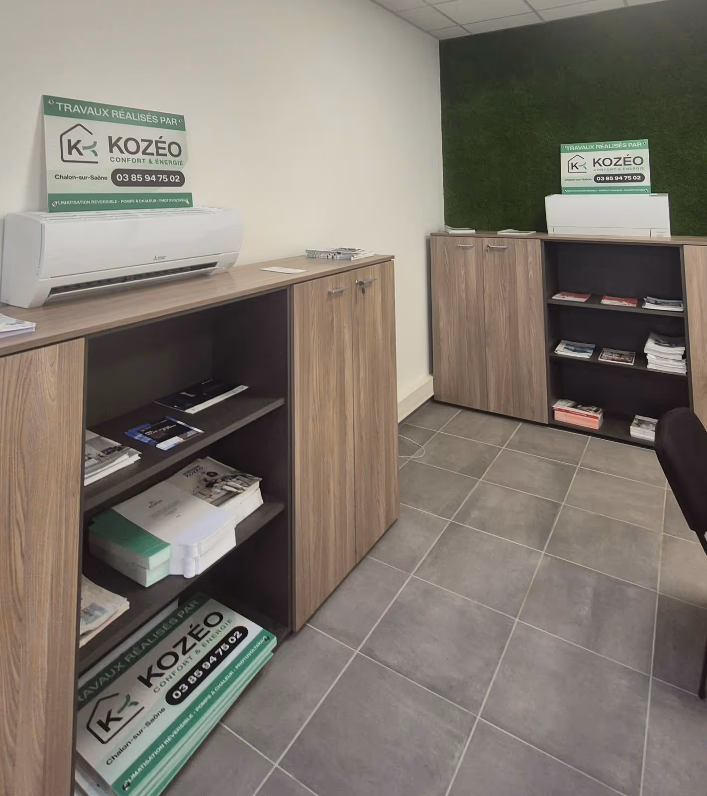 Coin bureau avec deux armoires en bois contenant des brochures et deux climatiseurs muraux avec un panneau publicitaire Kozéo.