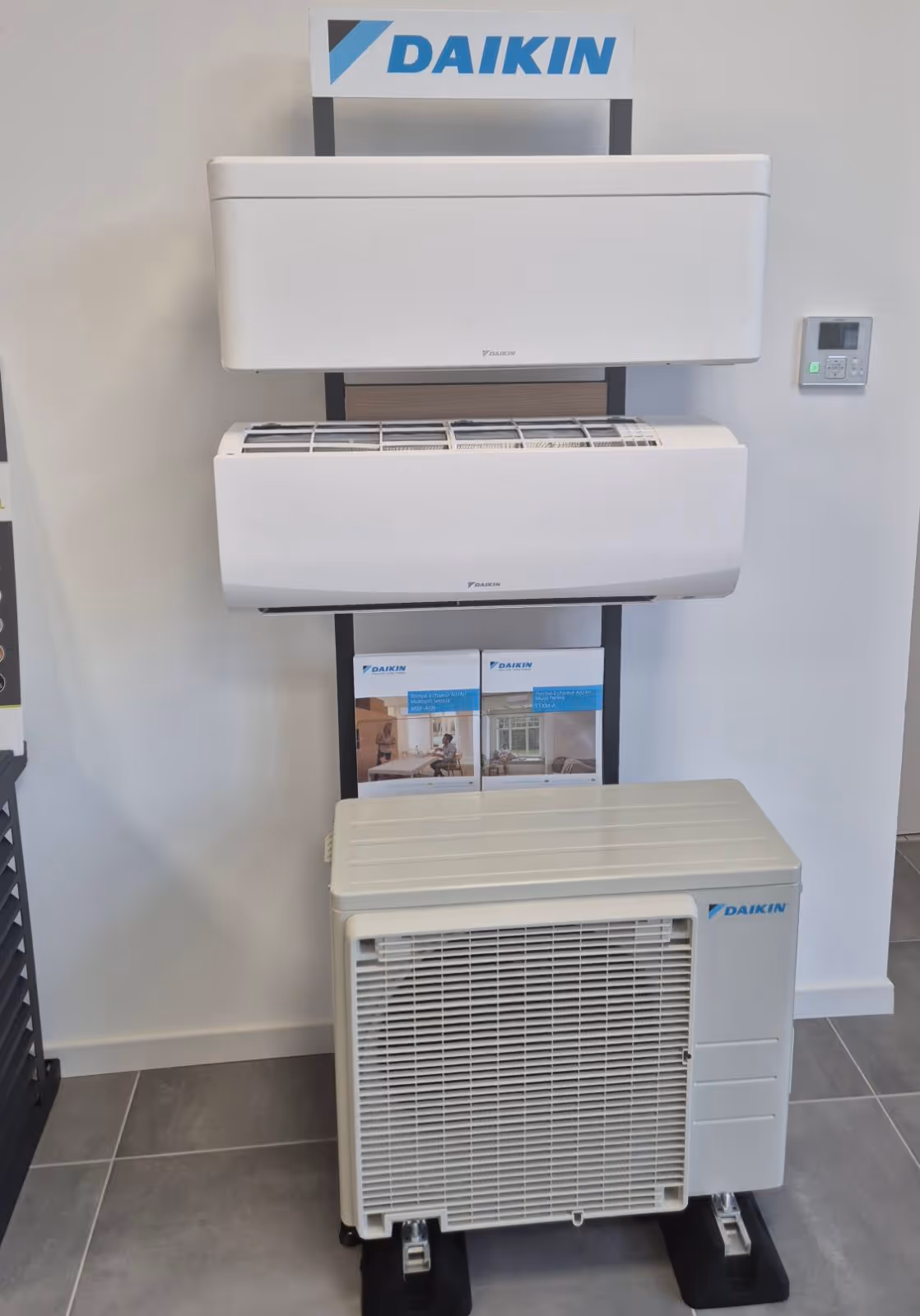Unités murales blanches Daikin et unité extérieure Daikin présentées sur un support intérieur avec une télécommande murale à côté.