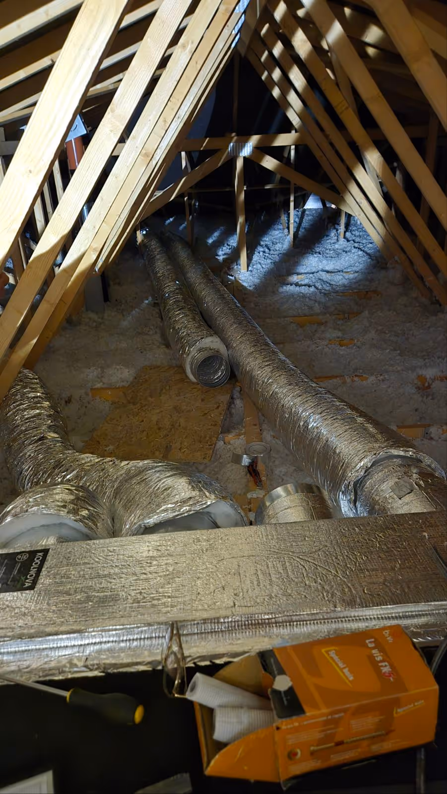 Conduits isolés en aluminium dans un grenier avec des chevrons en bois et isolation au sol.