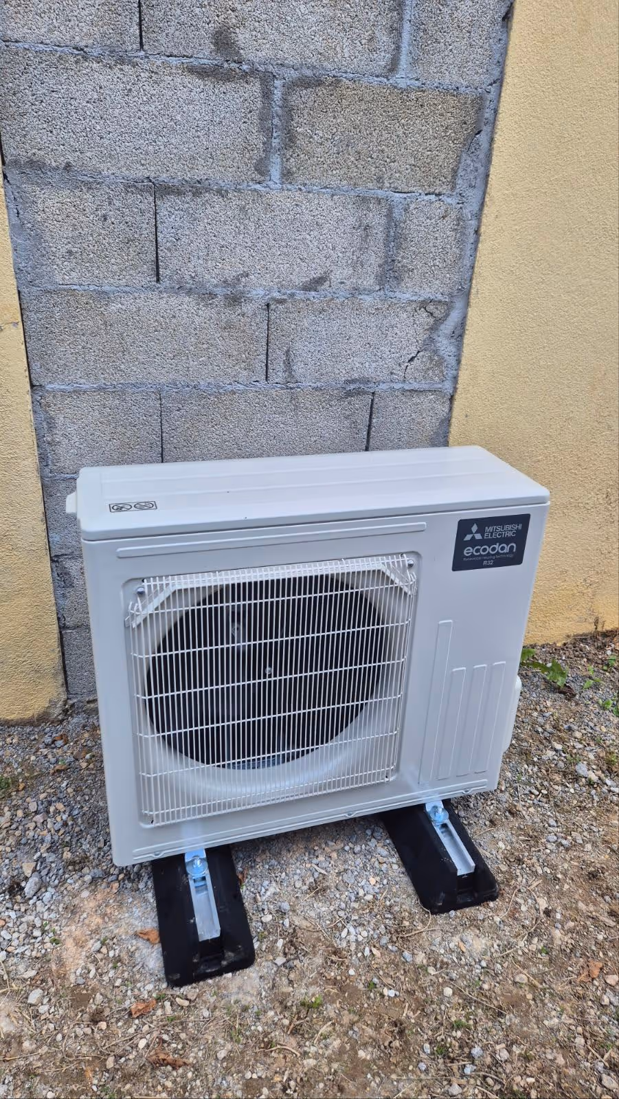 Unité extérieure d'une pompe à chaleur Mitsubishi Electric Ecodan installée contre un mur en parpaings.