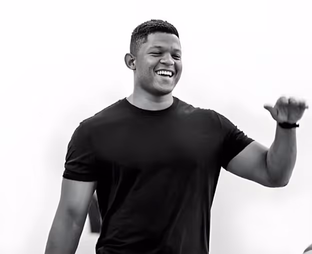 Smiling man in a black t-shirt gesturing with his right hand against a white background.