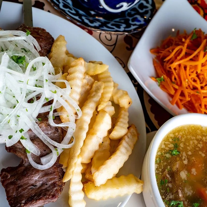 A plate of food with a bowl of soup and a plate of fries.