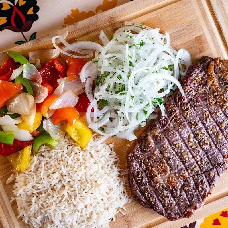 A plate of food with rice, onions, peppers, and meat.