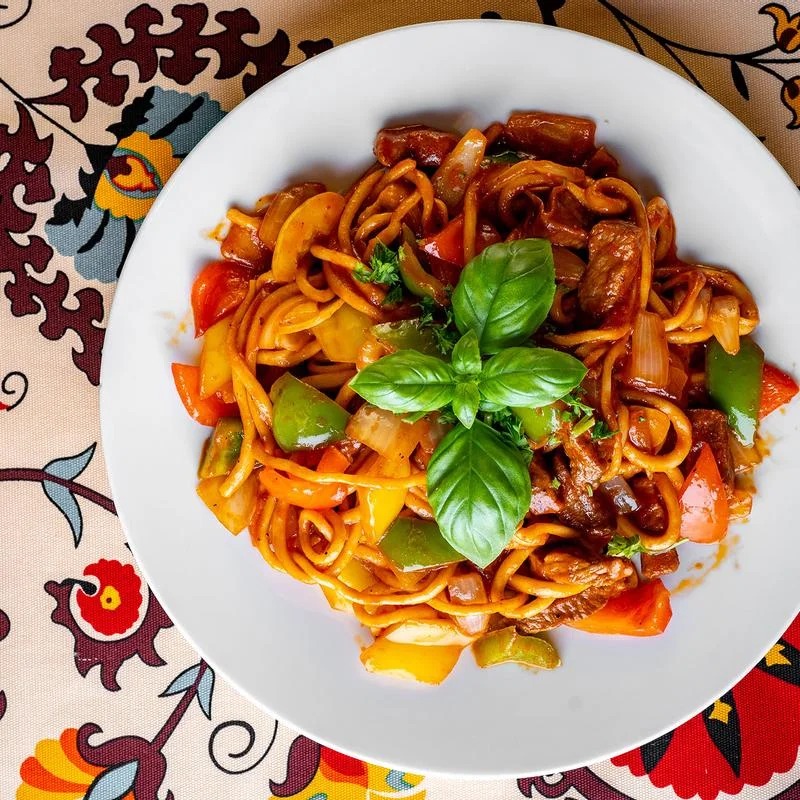 A plate of spaghetti topped with meat and colorful vegetables, garnished with herbs.
