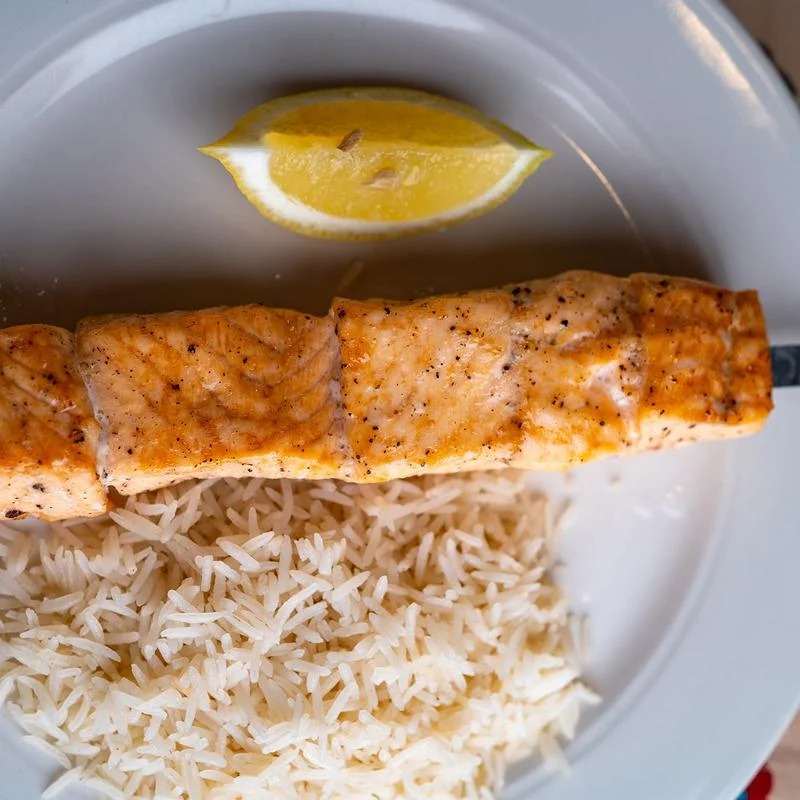 A plate of rice and salmon with a lemon wedge on top.