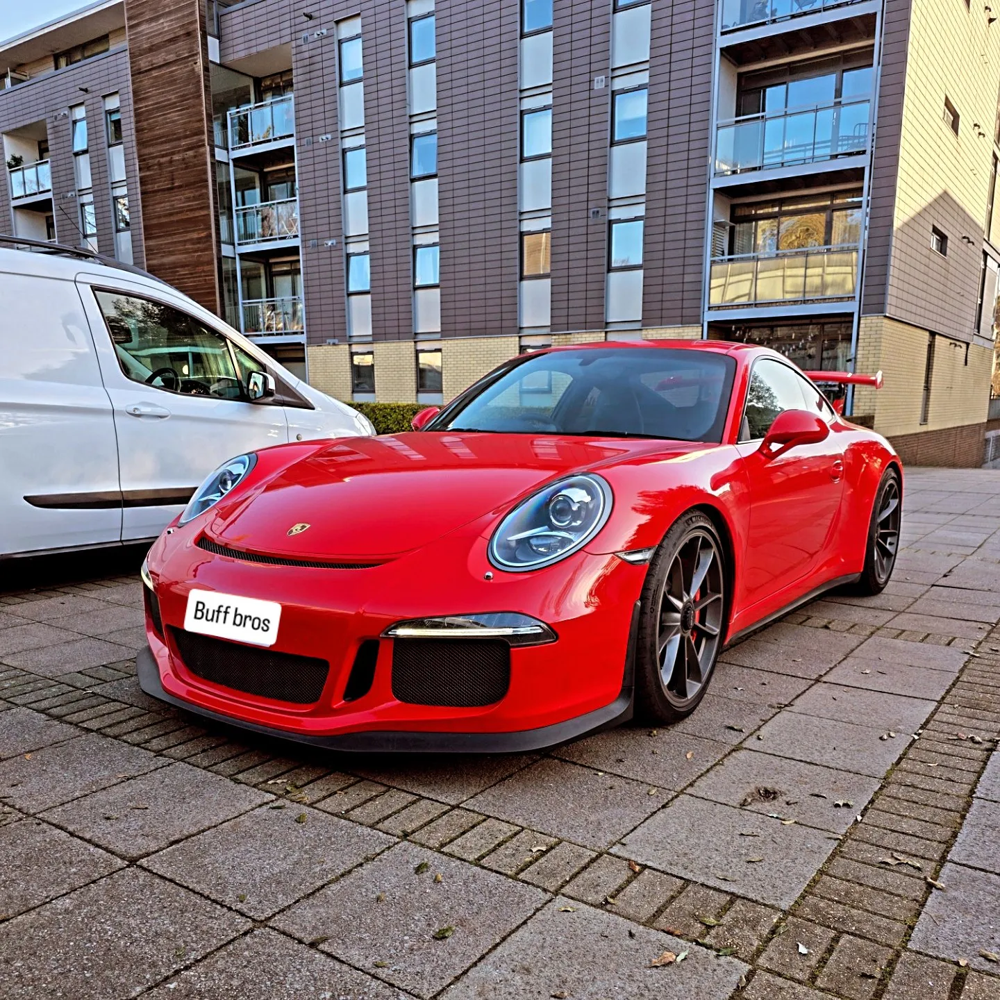 Red sports car parked on a paved street in front of a modern apartment building.