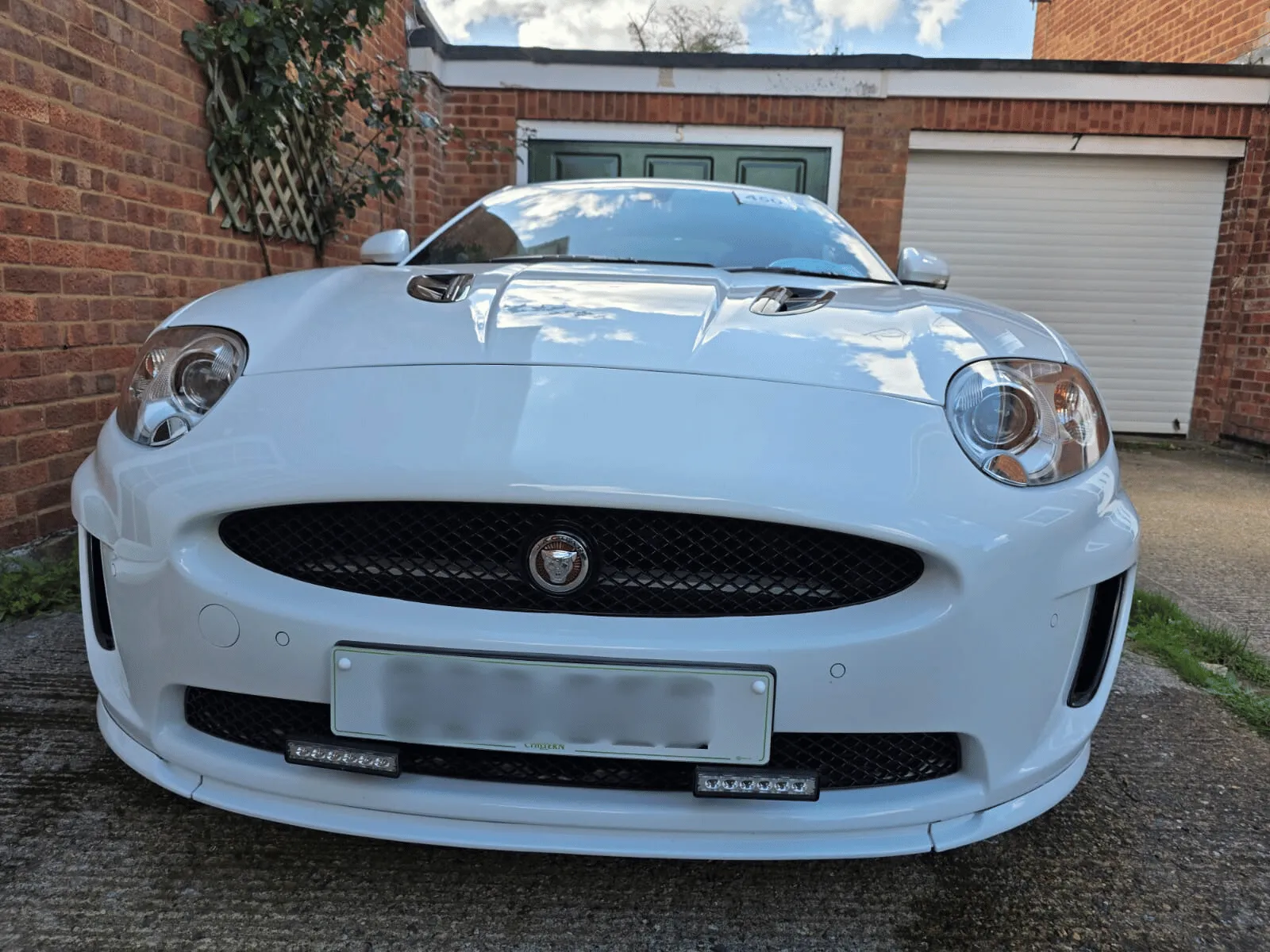 Front view of a white Jaguar car parked on a driveway with brick walls in the background.
