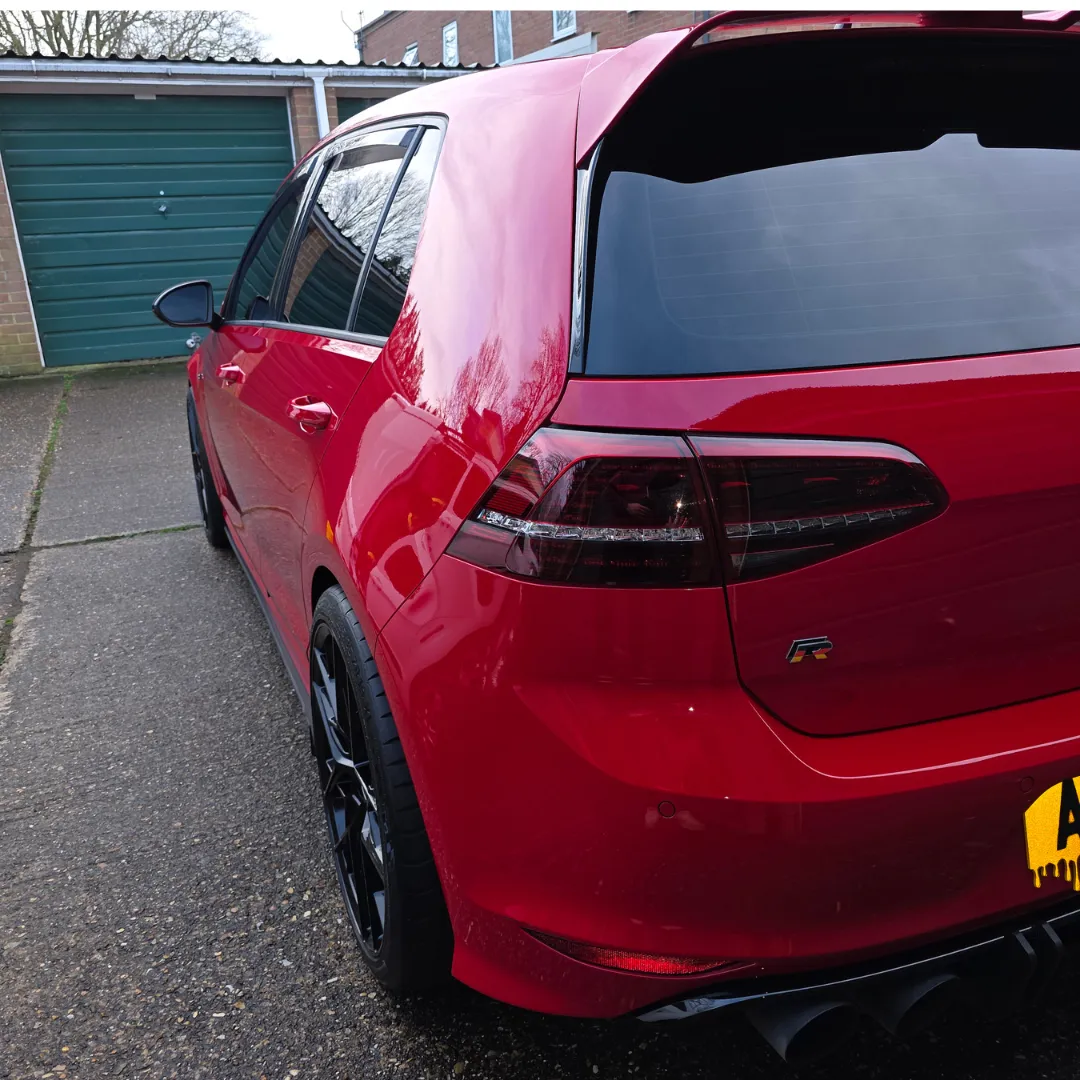 Rear-side view of a red Volkswagen Golf R hatchback parked on a driveway with black wheels and tinted rear lights.