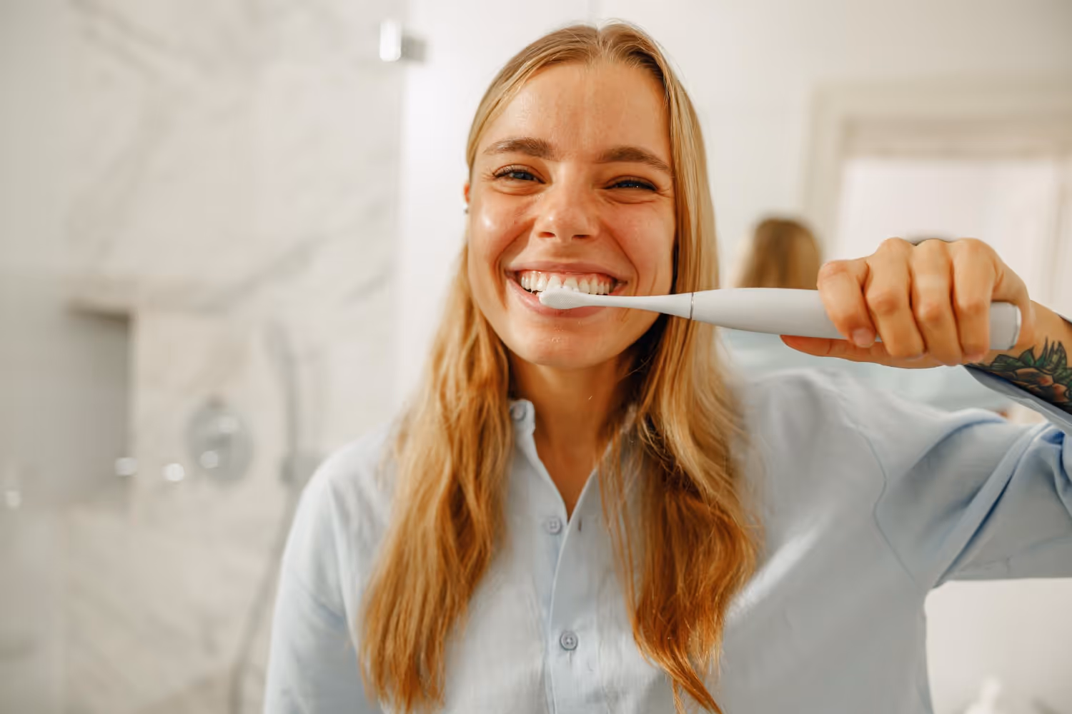 Junge Frau mit strahlendem Lächeln putzt ihre Zähne mit einer elektrischen Zahnbürste – gesunde Zahnpflege zu Hause, ergänzend zur professionellen Dentalhygiene bei Dübi Dental.
