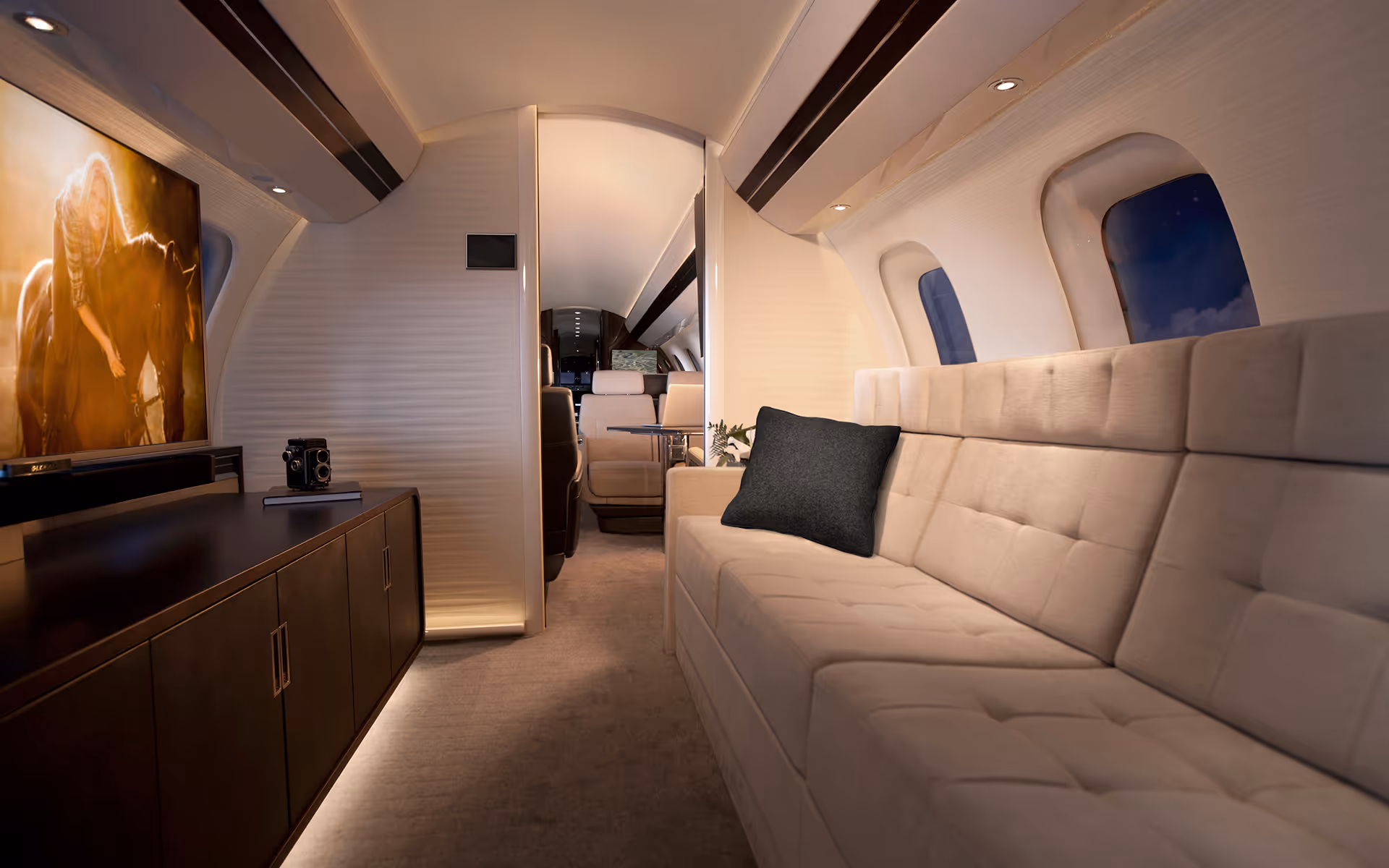 Interior of a private jet featuring a beige tufted sofa with a dark pillow, dark wooden cabinet with a vintage camera, and a large screen displaying an image of a woman with a horse.