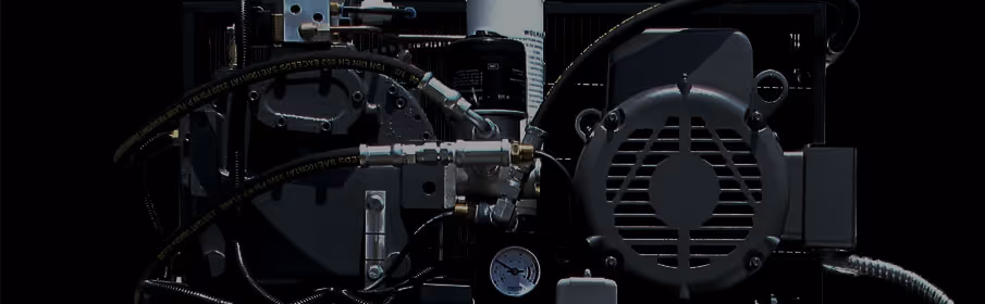 Close-up view of an industrial machine component with hoses, a pressure gauge, and a vented motor cover against a dark background.