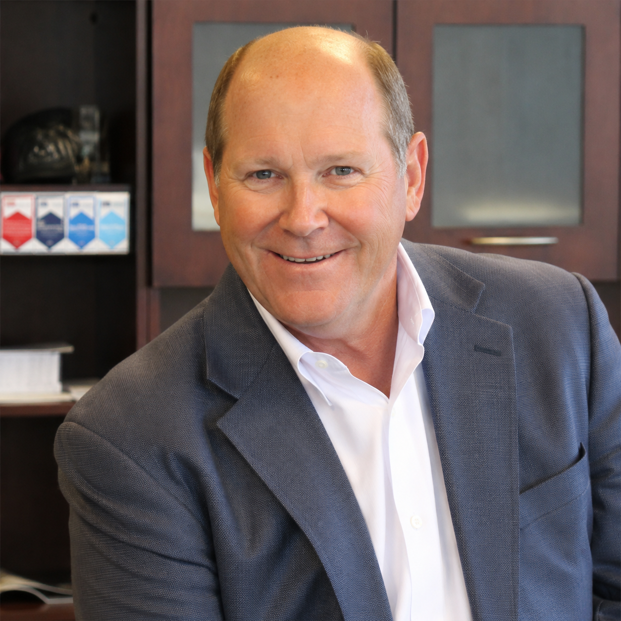 Smiling man in a grey suit, white shirt, in an office setting