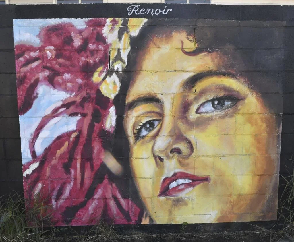 Vibrant mural shows a confident woman’s face with red feathers and “Renoir” above.