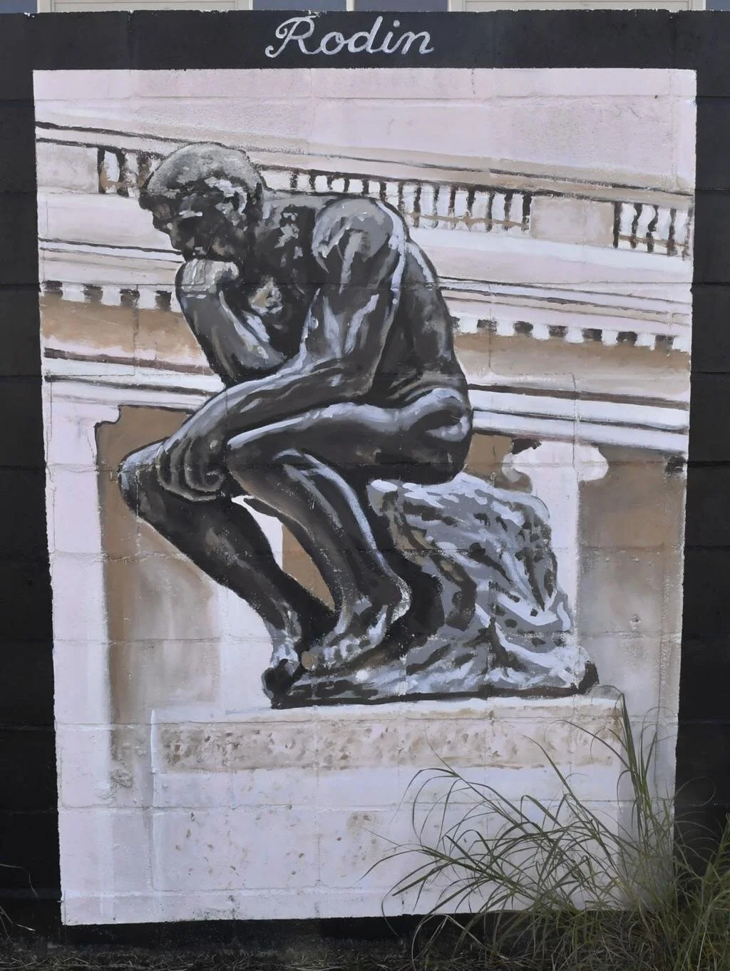 Mural of Rodin's "The Thinker" on a black wall, depicting a contemplative figure with a fist under chin, set against a classical building backdrop.