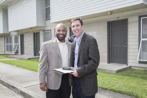 Two men pose smiling outside a brick apartment building during the event.