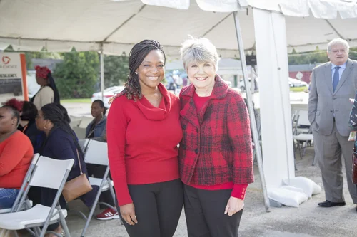 Two women pose together smiling under a white tent at an event.