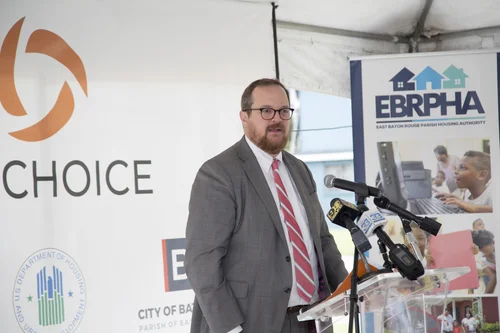 Man in grey suit and glasses speaks at podium with BR Choice and EBRPHA logos in background.