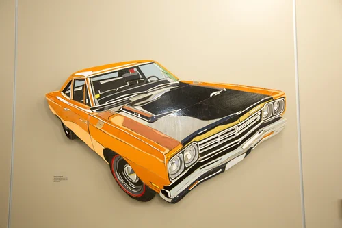Wall-mounted artwork of a classic orange muscle car with a black hood.