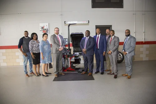 Group of officials poses next to automotive machinery inside a training center workshop.